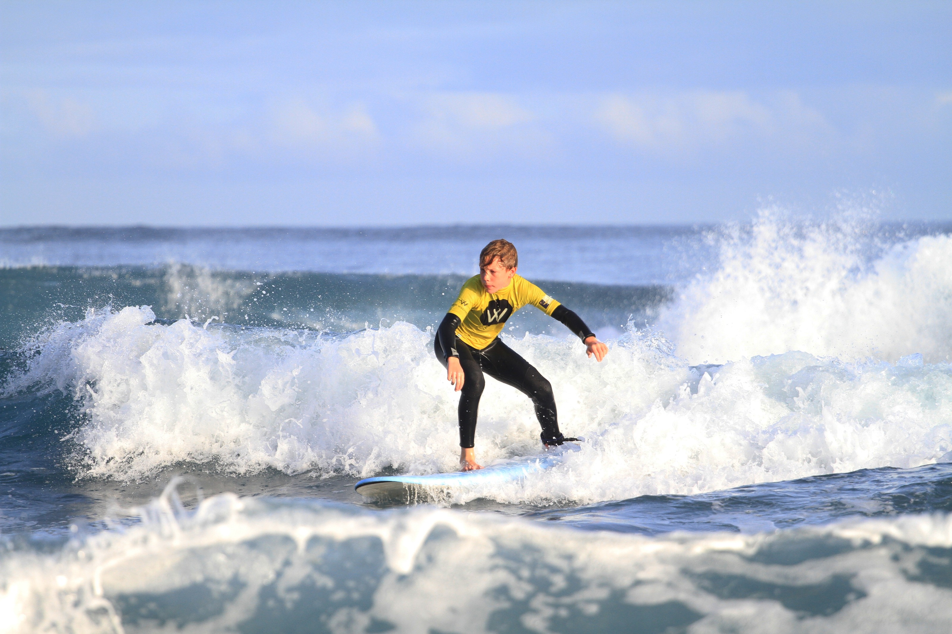 Niño con licra amarilla surfeando la espuma de la ola